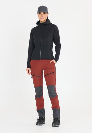 Zwarte ritsjack met textuurpanelen, gecombineerd met rode broeken met grijze accenten en ritszakken. Gekozen met zwarte schoenen.