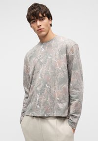 Πουκάμισο με μακριά μανίκια σε ανοιχτό γκρι χρώμα που διαθέτει καμουφλάζ εμπνευσμένο από τη φύση με απαλά καφέ και πράσινα χρώματα. Απαλό ύφασμα, άνετη γραμμή.