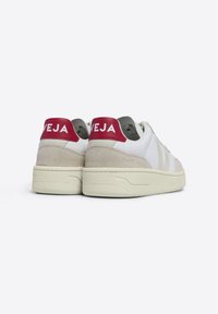Baskets blanches et beige avec un talon en daim texturé et un logo "VEJA" rouge et blanc audacieux à l'arrière, dotées d'une semelle épaisse et rembourrée.