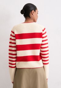 Pull rayé en mélange de laine crème et rouge. Présente de larges rayures horizontales, un ourlet côtelé et des manches longues avec des largeurs de rayures variées.