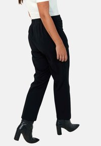 Black tapered pants with an elastic waistband, featuring a smooth texture and designed with a relaxed fit. Worn with black heeled ankle boots.