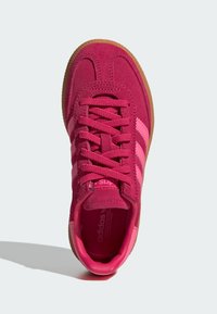 Rosa samt sportsko med rosa snører og tre kontrasterende lyserosa striper. Rund tå og gummisåle.