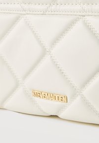 Λευκή καπιτονέ δερμάτινη τσάντα με διαγώνιες ραφές και μικρή χρυσή πλάκα με το λογότυπο "Steve Madden".