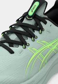 Scarpa da corsa blu chiaro con lacci neri, tomaia testurizzata e dettagli verde neon. Presenta una suola ammortizzata e un tallone rinforzato.