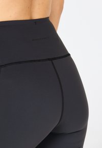 Leggings neri a vita alta realizzati in materiale liscio ed elastico, caratterizzati da cuciture a contrasto, una banda in vita ampia e un logo del brand discreto.