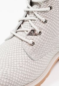 Botte grise texturée avec un motif reptile, équipée d'œillets métalliques argentés et de lacets blancs, ainsi que d'une semelle en caoutchouc clair.