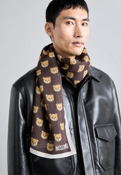 Fular maro cu un imprimeu repetitiv de urși în galben, fabricat dintr-un material moale. Accent alb la margine cu eticheta "MOSCHINO".