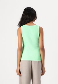 Green ribbed tank top with a round neckline and wide shoulder straps, paired with light beige trousers. Smooth texture, fitted design.