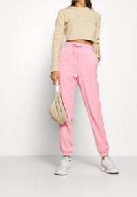 Beskuren långärmad beige topp med ribbat mönster, kombinerad med ljusrosa fleece-joggingbyxor med elastiska muddar och dragsko i midjan.