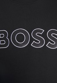 Černá mikina s výrazným bílým vyšitým nápisem "BOSS." Tkanina je texturovaná, s žebrovaným výstřihem a přiléhavým střihem.