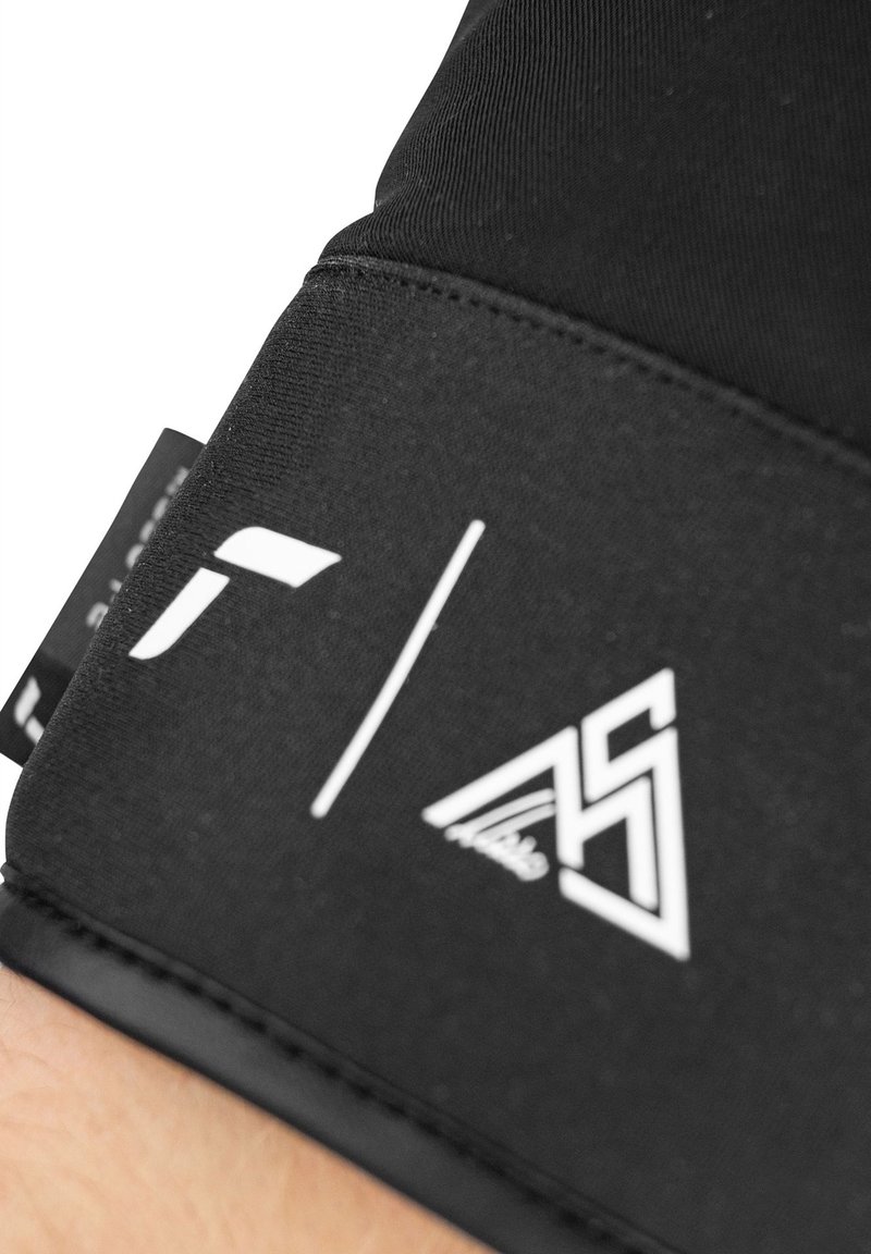 Guanto in tessuto nero con una superficie liscia, caratterizzato da loghi bianchi sul polsino. Elementi di design notevoli includono un bordo cucito e un'etichetta.