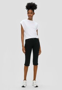 T-shirt blanc à manches courtes, coupe décontractée ; associé à un jean noir raccourci avec des poignets retroussés ; porté avec des baskets blanches.