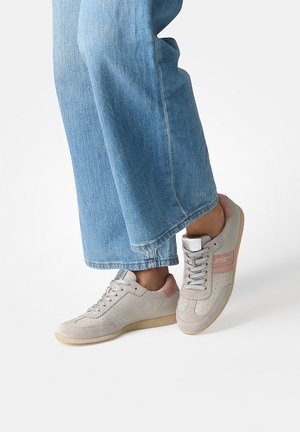 Person wearing light blue denim jeans and beige sneakers with pink accents, standing on a white background.
