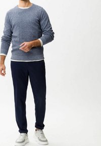 Niebieski sweter z dzianiny o fakturowanym wykończeniu, zestawiony z granatowymi spodniami chino i białymi tenisówkami. Sweter ma okrągły dekolt i długie rękawy.