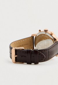 Orologio da polso con cinturino in pelle marrone, fibbia e cassa in oro rosa, che mostra il retro dell'orologio con dettagli visibili del marchio e del modello.