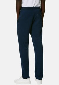 Pantalones de chándal azul marino con cintura elástica, bolsillos laterales y un bolsillo trasero. El material parece suave y flexible. Se llevan con zapatos blancos.