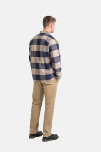 Camisa de franela a cuadros en azul marino y beige, con un frente abotonado y mangas largas. Combinada con pantalones caquí claros y zapatos negros.