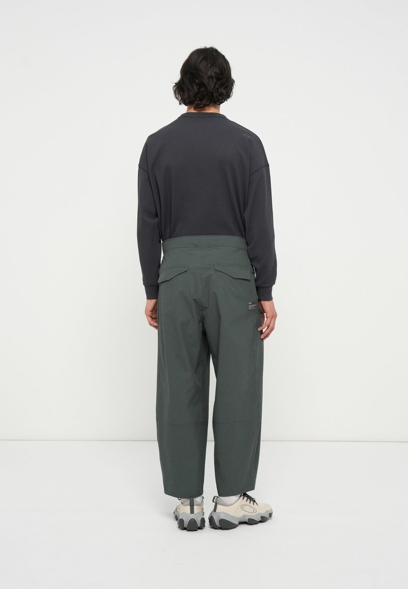 Sweatshirt gris surdimensionné avec texture côtelée, associé à un pantalon large vert avec des poches latérales. Les chaussures comprennent des baskets beiges.