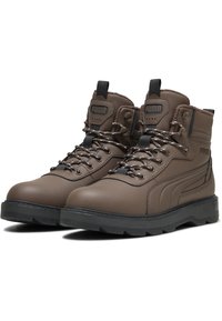 Stivaletti in pelle marrone con finitura testurizzata, suola in gomma nera, punta rinforzata, occhielli in metallo e lacci a contrasto. Logo PUMA sulla linguetta.