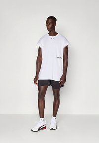 Bílé oversized tričko s krátkými rukávy, s malým černým logem. Kombinováno s černými šortkami a bílými teniskami s červenými detaily.