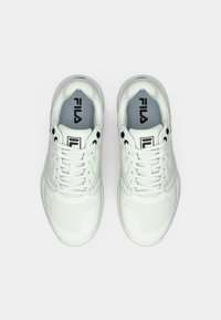 Tīru baltu FILA sporta apavu pāris, skatīts no augšas, redzami šņorēšanas elementi, zīmola logo uz mēles un iekšējās zoles uz baltas fona.