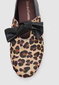 Zapato con estampado de leopardo que presenta un lazo de cuero negro, una puntera redondeada y un material superior texturizado similar al cuero. Branding dorado en la plantilla.