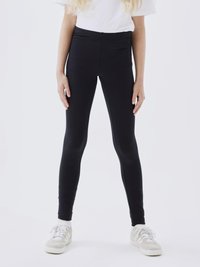 Zwarte leggings met een naadloos ontwerp, gemaakt van rekbaar materiaal. Gecombineerd met een plain wit t-shirt en lichtgekleurde sneakers.