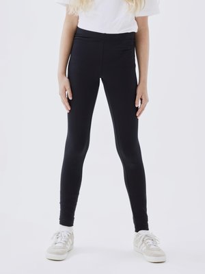 Leggings negre cu un design fără cusături, fabricate dintr-un material elastic. Combinat cu un tricou alb simplu și adidași de culoare deschisă.