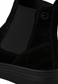 Bottine en suede noir avec des panneaux latéraux élastiques, semelle en caoutchouc noir texturé et détails cousus le long des bords.