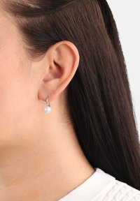 Orecchino a cerchio in argento con una perla bianca. La perla è rotonda e lucida, attaccata a un design di cerchio semplice e elegante, indossato in un piercing al lobo.