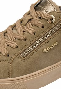 Olivza zaļa zamša sneaker ar bēšām šņorēm un ar rāvējslēdzēja akcentu. Iezīmēts ar zelta toņa logo un teksturētu gumijas zoli.