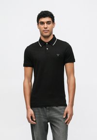 Μαύρο πόλο πουκάμισο με στενή γραμμή, διαθέτει αντίθετο λευκό γιακά, πατιλέτα με δύο κουμπιά και μικρό τριγωνικό λογότυπο στο στήθος.