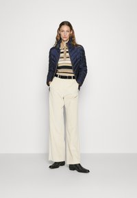 Marinblå kviltad jacka, beige randig polo, krämfärgade vida corduroybukser, och svarta stövletter, vilket skapar en lager på lager avslappnad outfit.