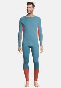 Maglietta termica a maniche lunghe in teal con dettagli rossi, abbinata a leggins coordinati con polsini rossi, realizzati in un materiale a maglia testurizzata.