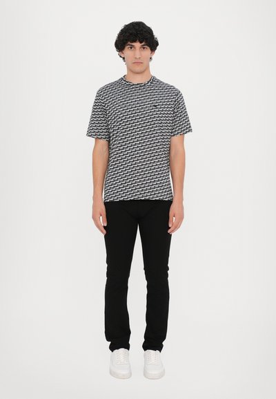 Short-sleeve t-shirt with a black and white wave pattern, paired with black skinny jeans and white sneakers. Simple, modern casual attire.