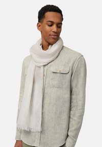 Écharpe légère blanche en tissu doux et texturé, drapée autour du cou, avec des extrémités frangées pour le détail, associée à une chemise grise.