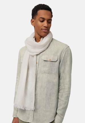Écharpe légère blanche en tissu doux et texturé, drapée autour du cou, avec des extrémités frangées pour le détail, associée à une chemise grise.