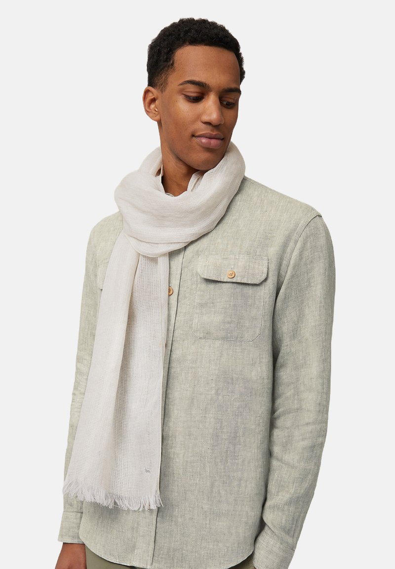 Écharpe légère blanche en tissu doux et texturé, drapée autour du cou, avec des extrémités frangées pour le détail, associée à une chemise grise.