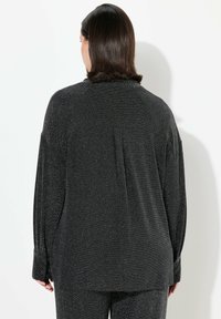 Zwarte lange mouwen top met metallic draaddetails, losse pasvorm en een klassieke kraag. Heeft knoopmanchetten en een geplooid achterontwerp.
