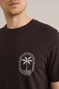 Bruine katoenen T-shirt met een witte geborduurde palmboomontwerp en tekst in een cirkelvormige omlijsting op de linkerkant van de borst.