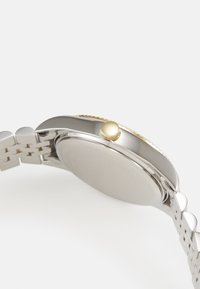 Orologio in acciaio inossidabile argentato con finitura lucida, corona con dettagli dorati e design a bracciale collegato. Cassa posteriore liscia e arrotondata.