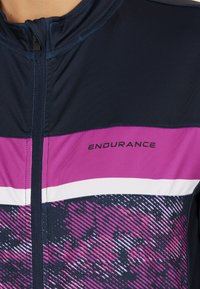 Marinblå sportjacka med rosa och vita horisontella ränder. Har en dragkedjeslutning och ett texturerat grafiskt mönster på den nedre delen.