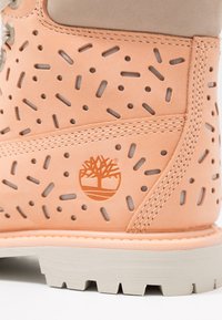 Stivale da adulto in pelle pesca con dettagli intagliati, accenti grigio chiaro e suola in gomma bianca testurizzata. Presenta un logo sul lato.