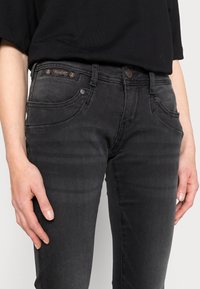 Svarta denimjeans med slim fit, med kontrasterande sömmar, femficksdesign och en logotypapplikation vid midjan.