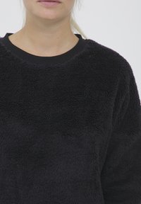Svart fleece-genser med en myk, teksturert overflate og ribbestrikket rund hals. Designet er enkelt og avslappet.
