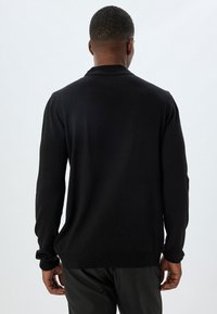 Schwarzer Pullover mit langen Ärmeln, tailliertem Design, gerippten Bündchen und glatter Textur, ausgestattet mit einem klassischen Kragen und einer leicht lockeren Passform.