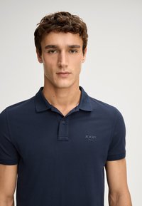Marineblauwe poloshirt van glad katoen, met een twee-knopen knoopsluiting, korte mouwen en een logoaccent op de linkerborst.