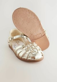 Gyldne metalliske sandaler med et vævet design, justerbar spænde-rem og en mønstret indersål. Sålen har et design med en enhjørning og stjerner.