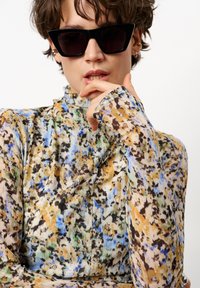 Multikleurige bloemenprint top met lange mouwen, hoge hals en gerimpelde details. De stof heeft tinten van blauw, bruin en groen.