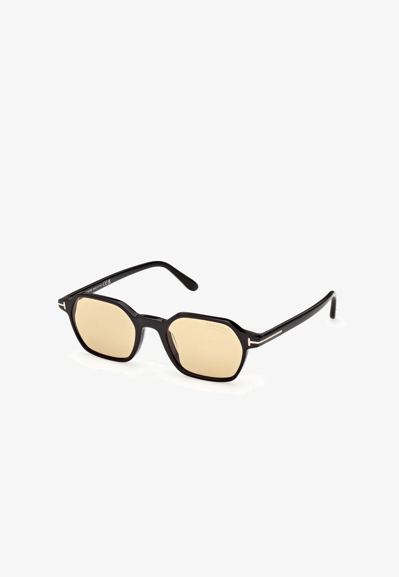 Mustat aurinkolasit, joissa on oktaalimuoto. Vaaleankeltaiset sävytetyt linssit ja hennot mustat varret, joissa on kultaiset yksityiskohdat. Logo edessä.